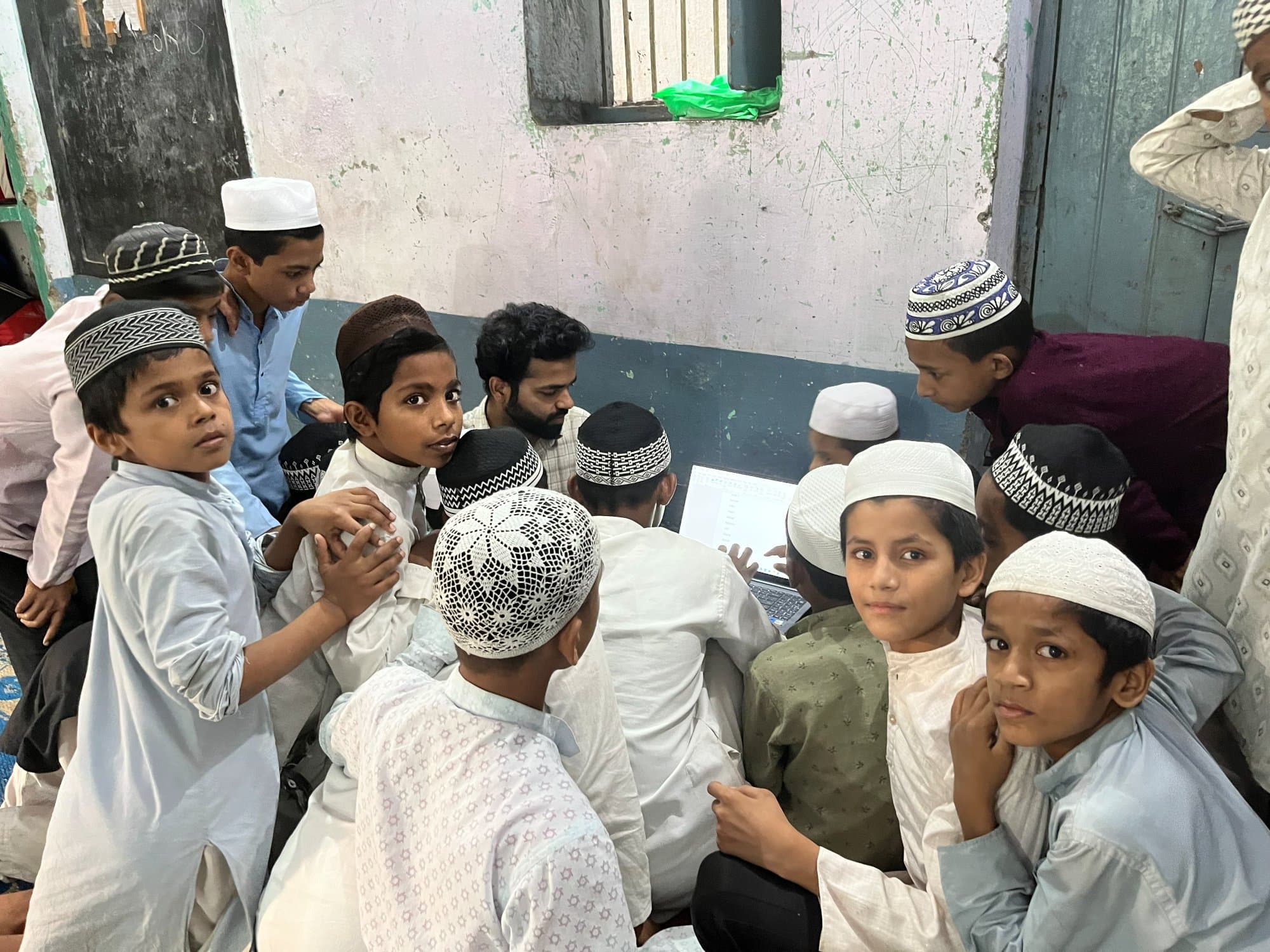 डिजिटल-साक्षरता सत्र के दौरान मदरसा छात्र, कुछ लैपटॉप स्क्रीन देखते हुए और कुछ कैमरे की ओर।